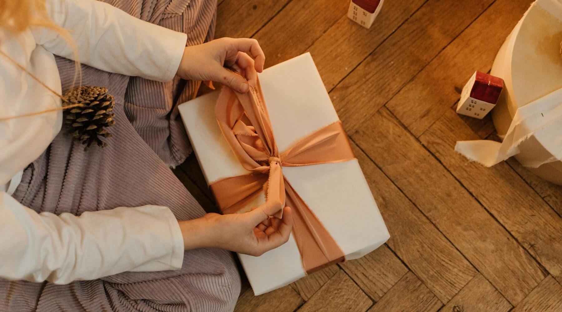 A person carefully tying a pink ribbon around a white wrapped gift, possibly one of many Christmas gift ideas for cat lovers.